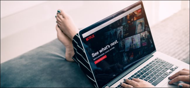 Os pés de uma mulher esticados em um banquinho enquanto ela navega no Netflix em um laptop.