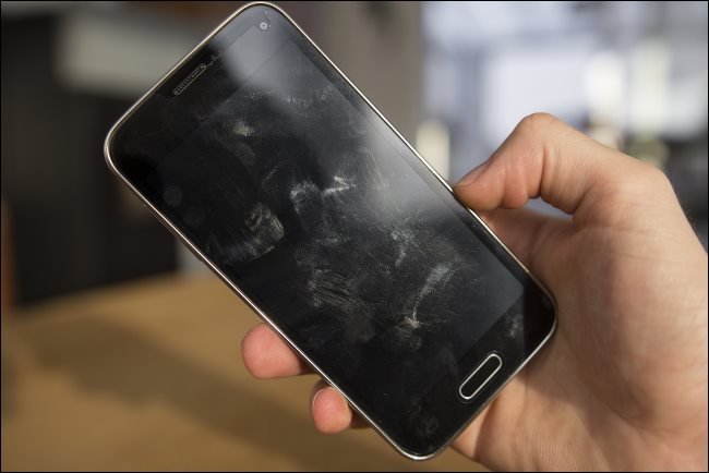 Uma mão segurando um telefone Android com manchas na tela.