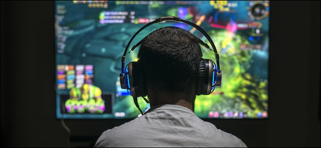 Um homem jogando videogame em um monitor ultra amplo, usando fones de ouvido.