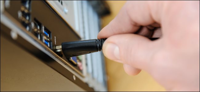 Uma mão conectando um cabo HDMI a um PC de mesa.