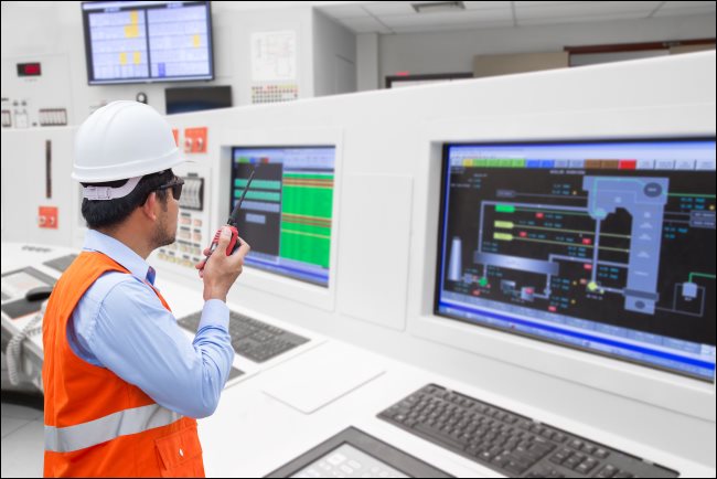 Um engenheiro elétrico na frente de computadores na sala de controle de uma usina termelétrica.