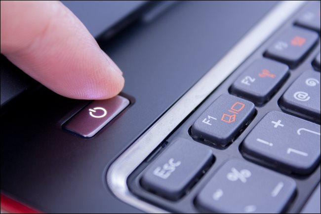 Um dedo pressionando o botão liga / desliga de um laptop PC para desligá-lo.