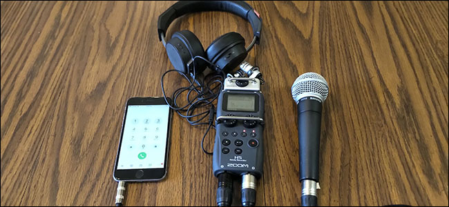 Um iPhone, microfone Shure SM58 e fones de ouvido, todos conectados a um gravador H5 Zoom, sobre uma mesa.