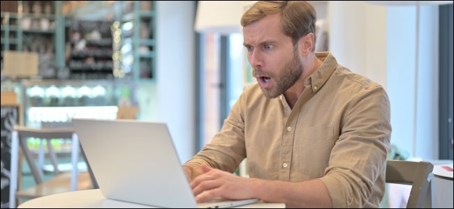 Um homem olhando para seu laptop com uma expressão chocada.