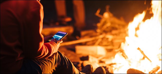 Uma pessoa usando um smartphone em frente a uma fogueira à noite.