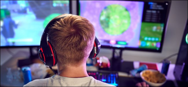 As costas de um menino, que está usando fones de ouvido e sentado em frente a um computador com dois monitores.