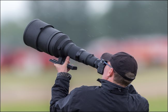 Um fotógrafo usando uma lente teleobjetiva enorme.