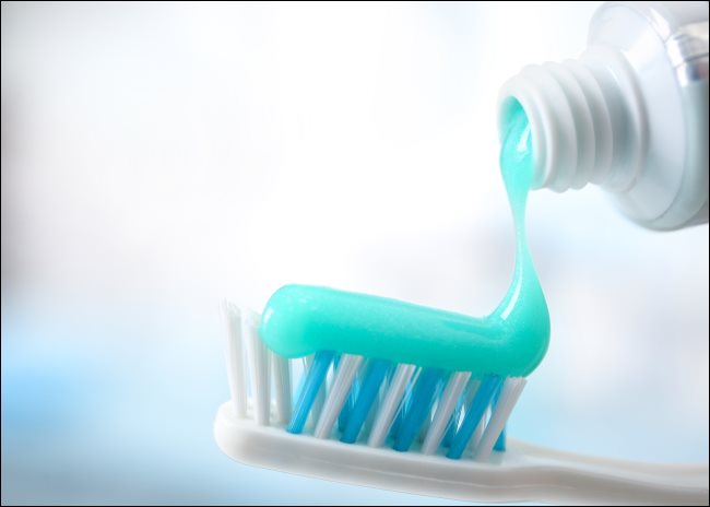 Pasta de dente sendo esguichada de um tubo para uma escova de dentes.