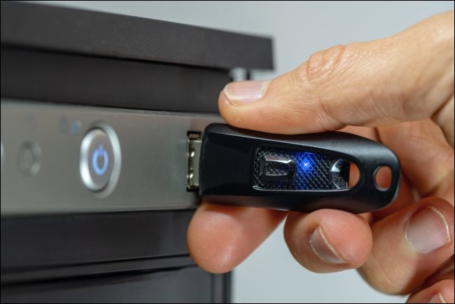 Uma mão inserindo uma unidade flash USB em um computador desktop.