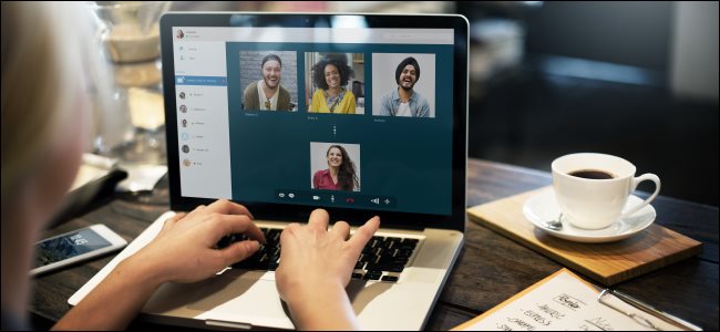 As mãos de uma mulher no teclado de seu laptop, com quatro pessoas em uma videoconferência na tela. 