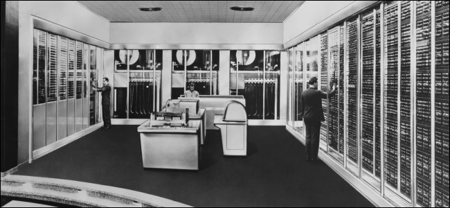 Três pessoas monitorando um computador mainframe antigo da era COBOL.