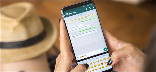 Mãos de mulher segurando um smartphone e digitando emojis no WhatsApp.