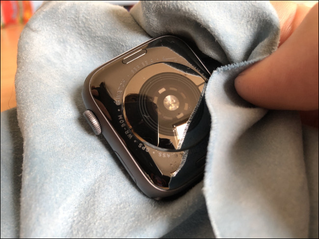 Uma mão limpando um Apple Watch com um pano.