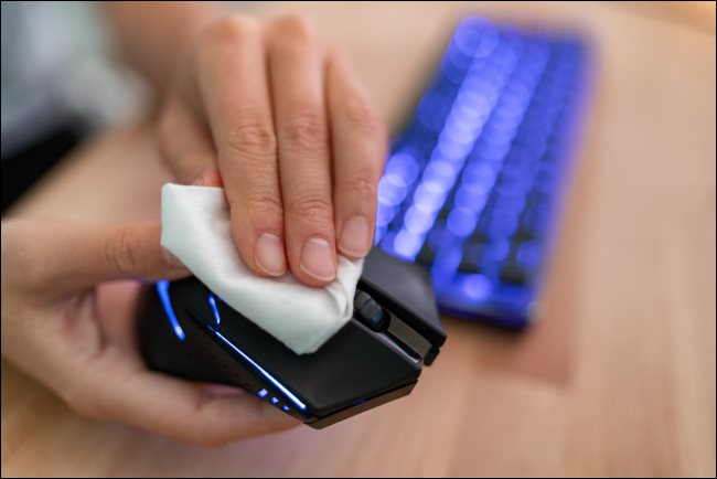 Uma mão limpando um mouse de computador com um pano.