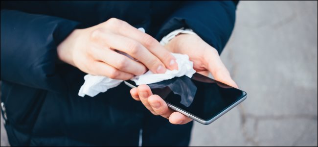 Mãos segurando e limpando a tela do smartphone com um pano.