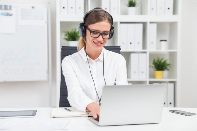 Uma mulher usando fones de ouvido e digitando em um laptop.