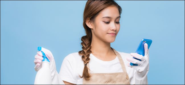 Uma jovem usando um smartphone enquanto segura produtos de limpeza.