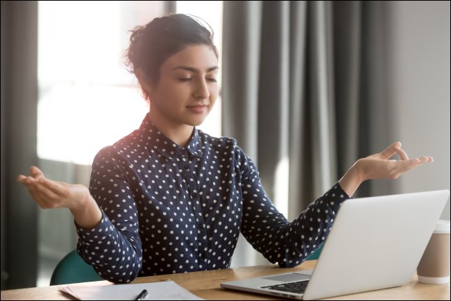 Uma mulher meditando na frente de um MacBook em um escritório.