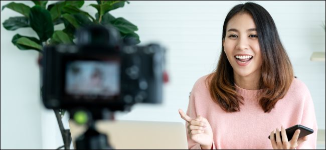 Uma mulher filmando um vídeo em uma câmera na frente de um laptop.