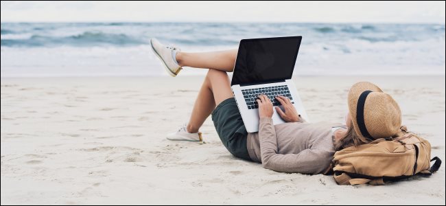 Uma mulher usando um laptop enquanto estava deitado na praia.