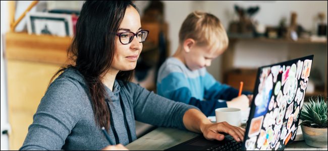 Uma mulher que trabalha em um laptop com uma criança sentada ao lado de seu desenho.