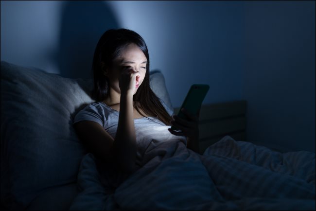 Uma mulher usando um smartphone na cama à noite.