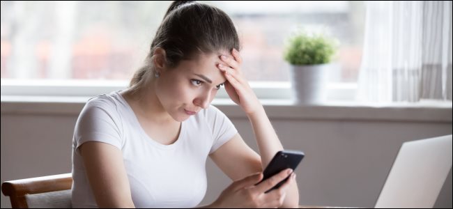 Uma jovem irritada segurando um smartphone e olhando para a tela do computador.