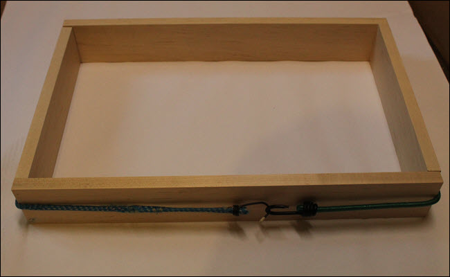 Quatro pedaços de madeira dispostos em um retângulo com uma corda elástica os puxando juntos.