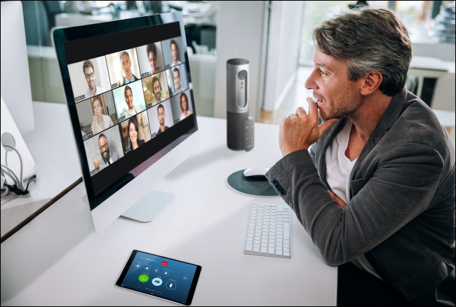 Um homem em uma reunião do Zoom em seu Mac com os participantes no Gallery View no monitor. 