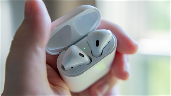 Uma mão segurando um par de Apple AirPods em sua caixa aberta.