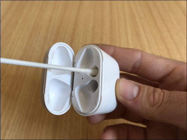 A mão de um homem segurando um estojo de carregamento AirPods e limpando os canais de carregamento com um cotonete.