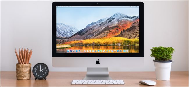 Um iMac com teclado e mouse da Apple em uma mesa de madeira.