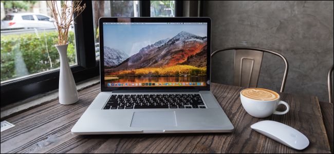 Um MacBook e um mouse Apple com uma xícara de café em uma mesa de madeira.
