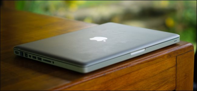 Um velho e grosso MacBook Pro sobre uma mesa de madeira.
