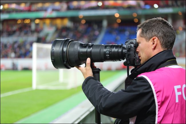 Um fotógrafo com uma grande lente de zoom óptico em um jogo de futebol.