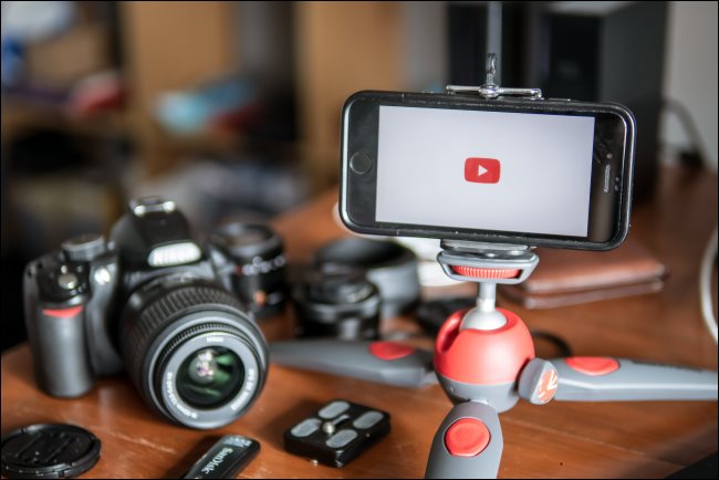 Uma câmera sobre uma mesa ao lado de um smartphone montado em um tripé de mesa.