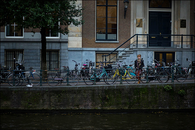 Uma mulher de pé em uma ponte atrás de uma fila de bicicletas estacionadas.