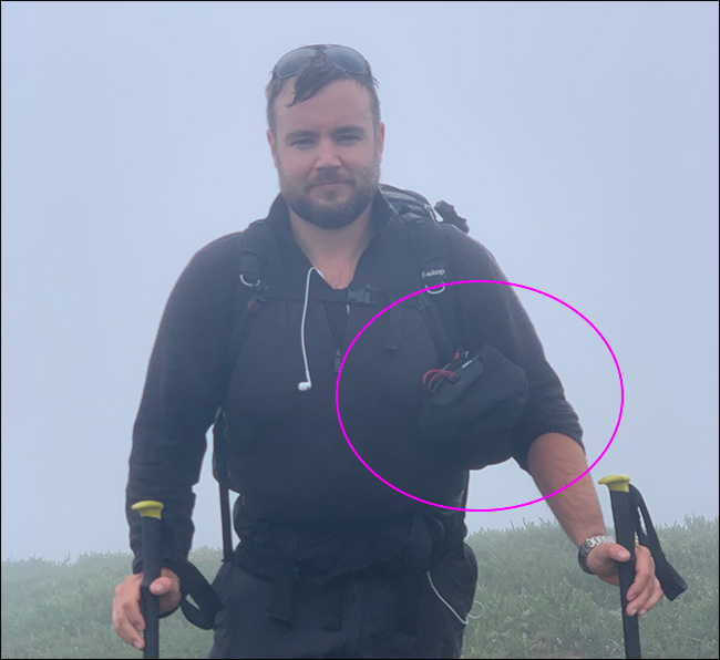 Um homem caminhando na chuva carregando um tripé e uma bolsa Peak Design Camera Shell.
