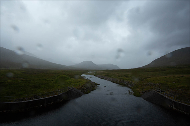 Uma foto chuvosa de uma montanha e um riacho com gotas de água na lente. 