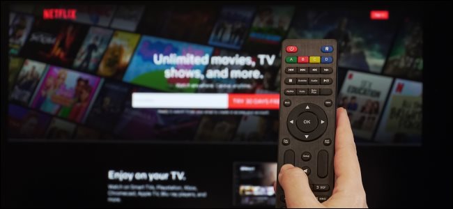 Uma mão segurando um controle remoto em frente à tela de inscrição da Netflix em uma TV.