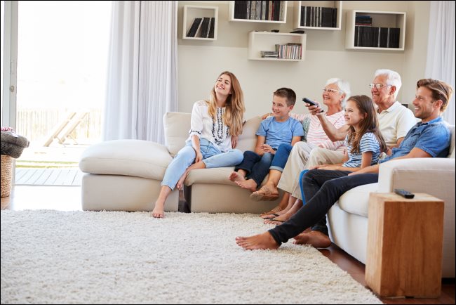 Uma família sentada em um sofá assistindo TV.