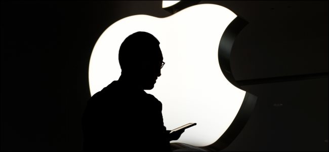 A silhueta de uma pessoa usando um iPhone na frente de um logotipo da Apple.