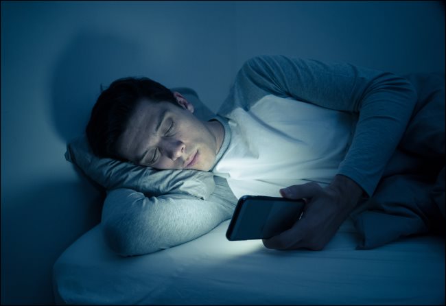Um homem enviando mensagens de texto em seu smartphone na cama à noite.