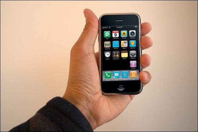 Uma mão segurando um iPhone de primeira geração.