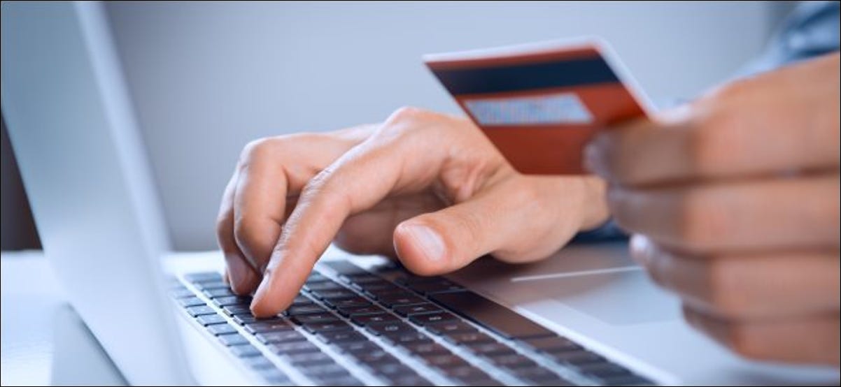 Uma pessoa segurando um cartão de crédito ou débito enquanto digita em um laptop.