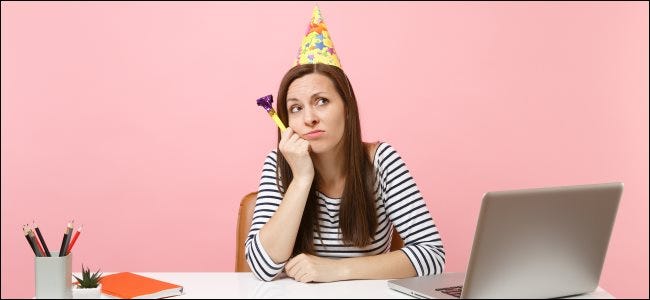 Uma pessoa com um chapéu de festa sentada sozinha em uma mesa.