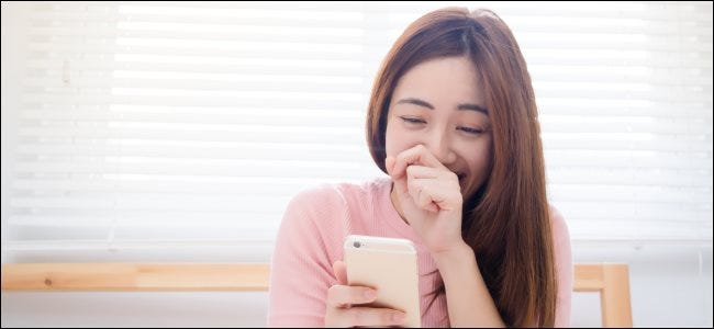 Uma pessoa rindo enquanto olha para um smartphone.