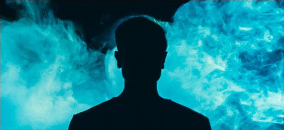 A silhueta de um indivíduo na frente de uma fumaça azul sobre um fundo escuro.
