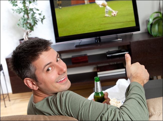 Um homem fazendo sinal de positivo em frente a uma TV.