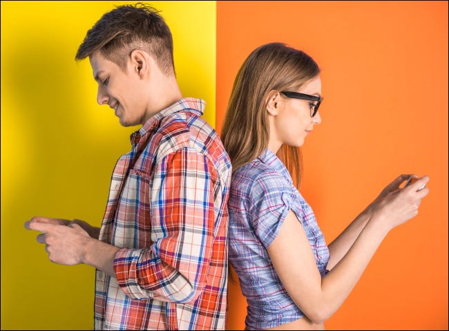 Um jovem casal em pé, costas com costas, ao usar seus telefones.